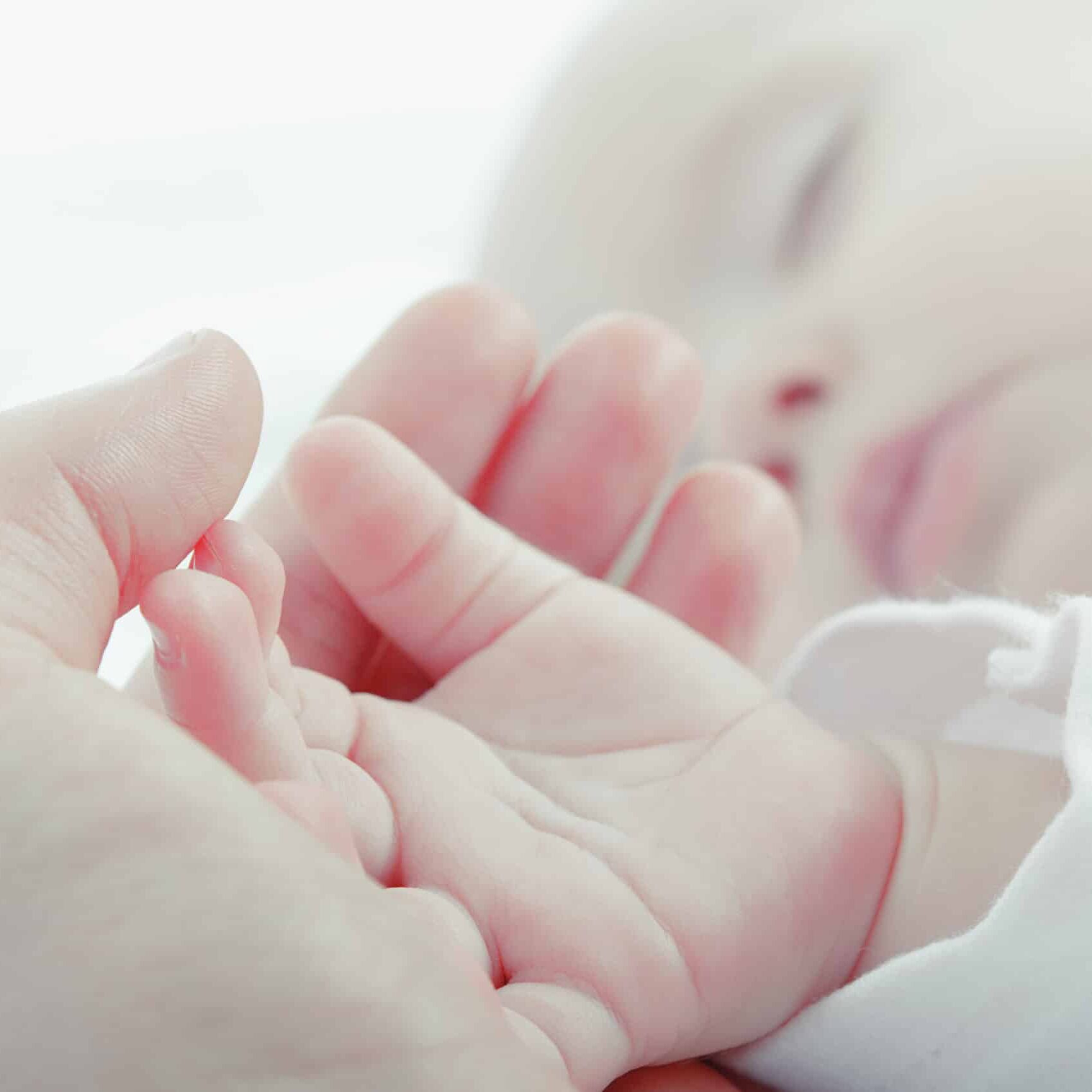 Baby sleeping with hand in adults hand.
